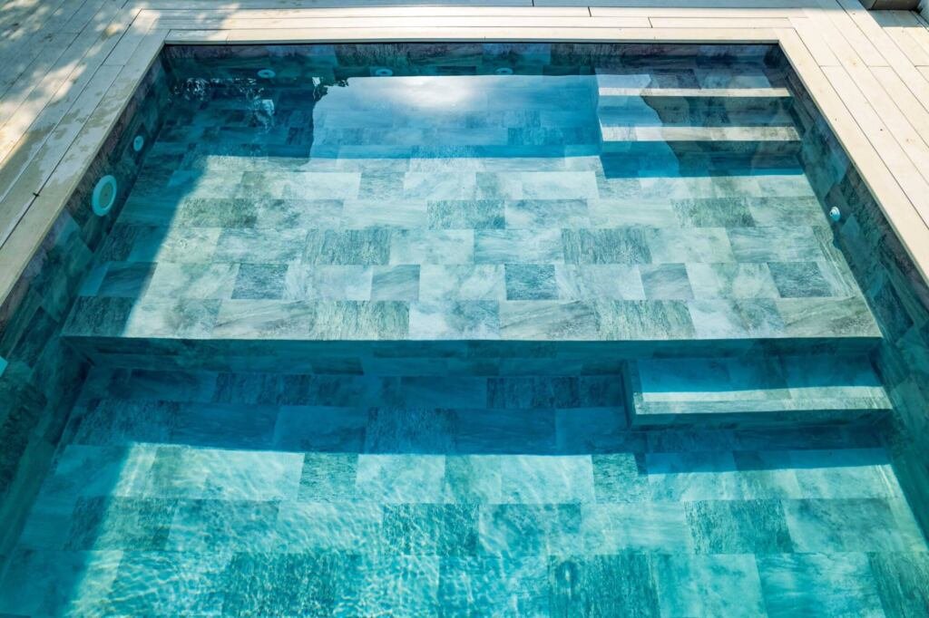 Piscina de obra moderna con revestimiento de liner, rodeada de un paisaje de jardín bien cuidado.